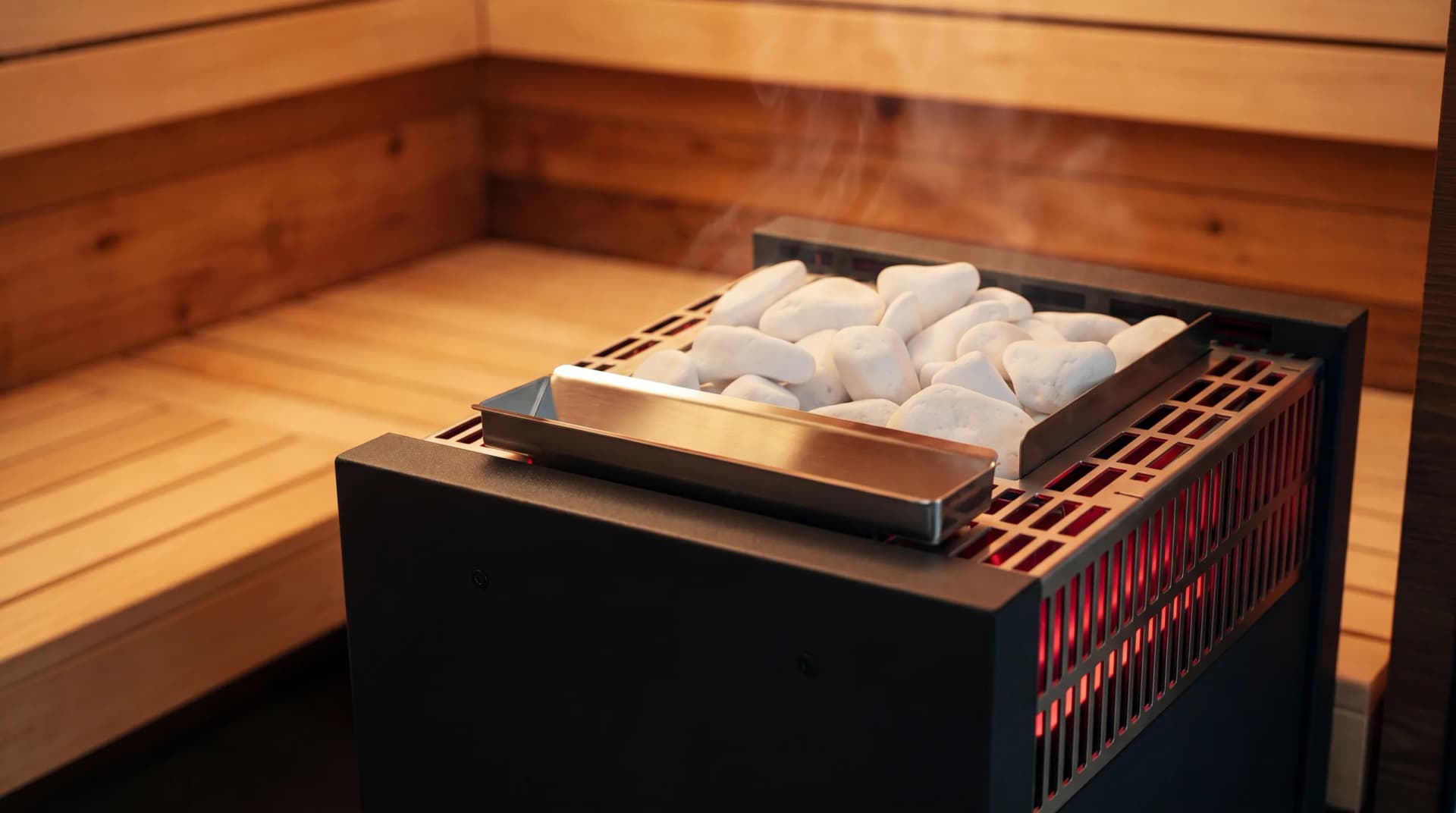 Premium Saunaofen mit weißen Saunasteinen, glühenden Heizstäben und Edelstahl-Verdunsterschale in einer warm beleuchteten Holzsauna – Saunaöfen und Zubehör von Hein Wellnesskonzepte